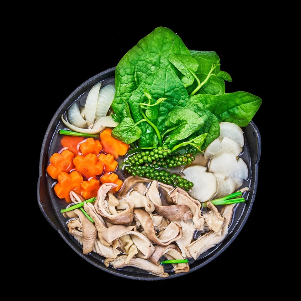 Vietnamese hot pot with green leafy vegetables, carrots, onions, mushrooms, and green peppercorns.