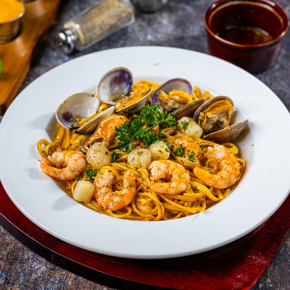 Oc Lau Nuong's seafood pasta with shrimp, clams, and scallops, garnished with parsley.
