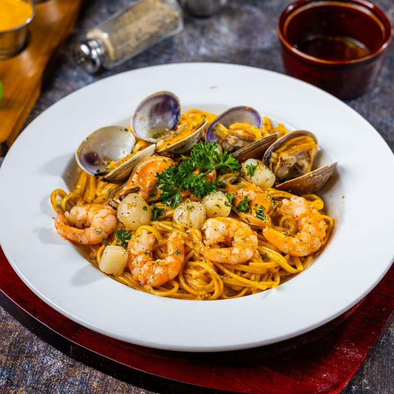 Oc Lau Nuong's seafood pasta with shrimp, clams, and scallops, garnished with parsley.