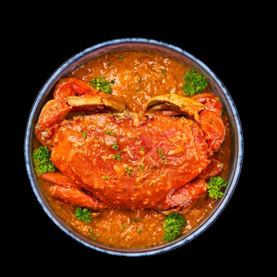 Whole crab in a rich, orange-red sauce, garnished with parsley in a blue bowl.