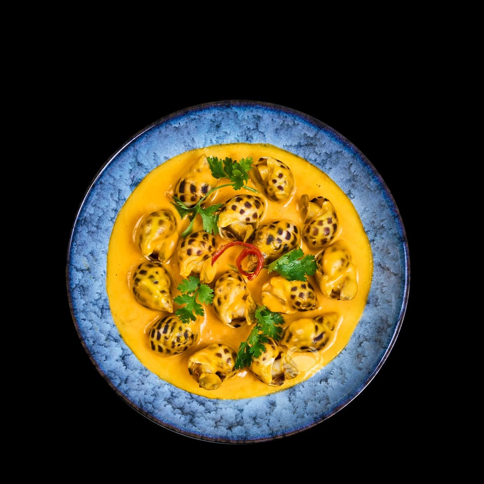 Vietnamese snails in a rich yellow sauce, garnished with cilantro and red chili, on a blue plate.