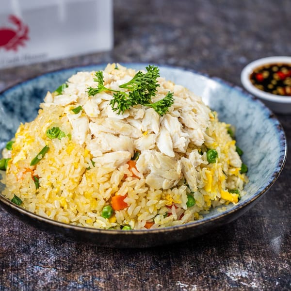 Crab fried rice with peas, carrots, and parsley in a blue bowl with a side of sauce.