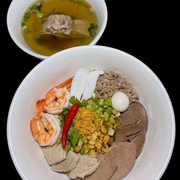 Vietnamese noodle dish with shrimp, squid, pork, egg, and herbs, served with a side of broth.