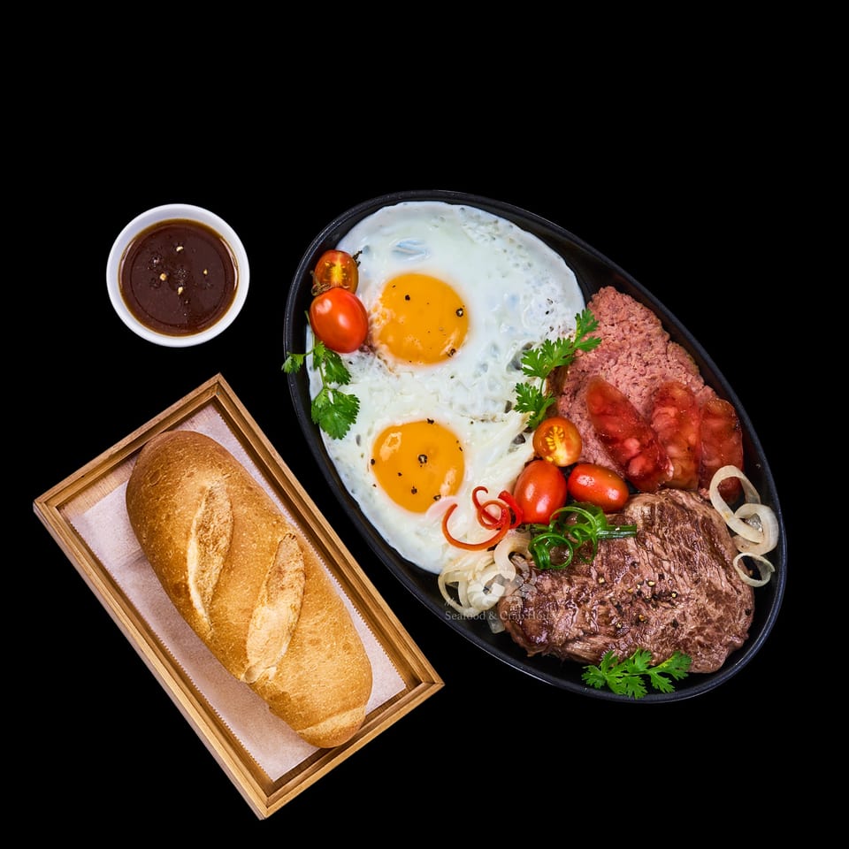 Vietnamese breakfast with fried eggs, steak, sausage, pate, tomatoes, onions, and a baguette.